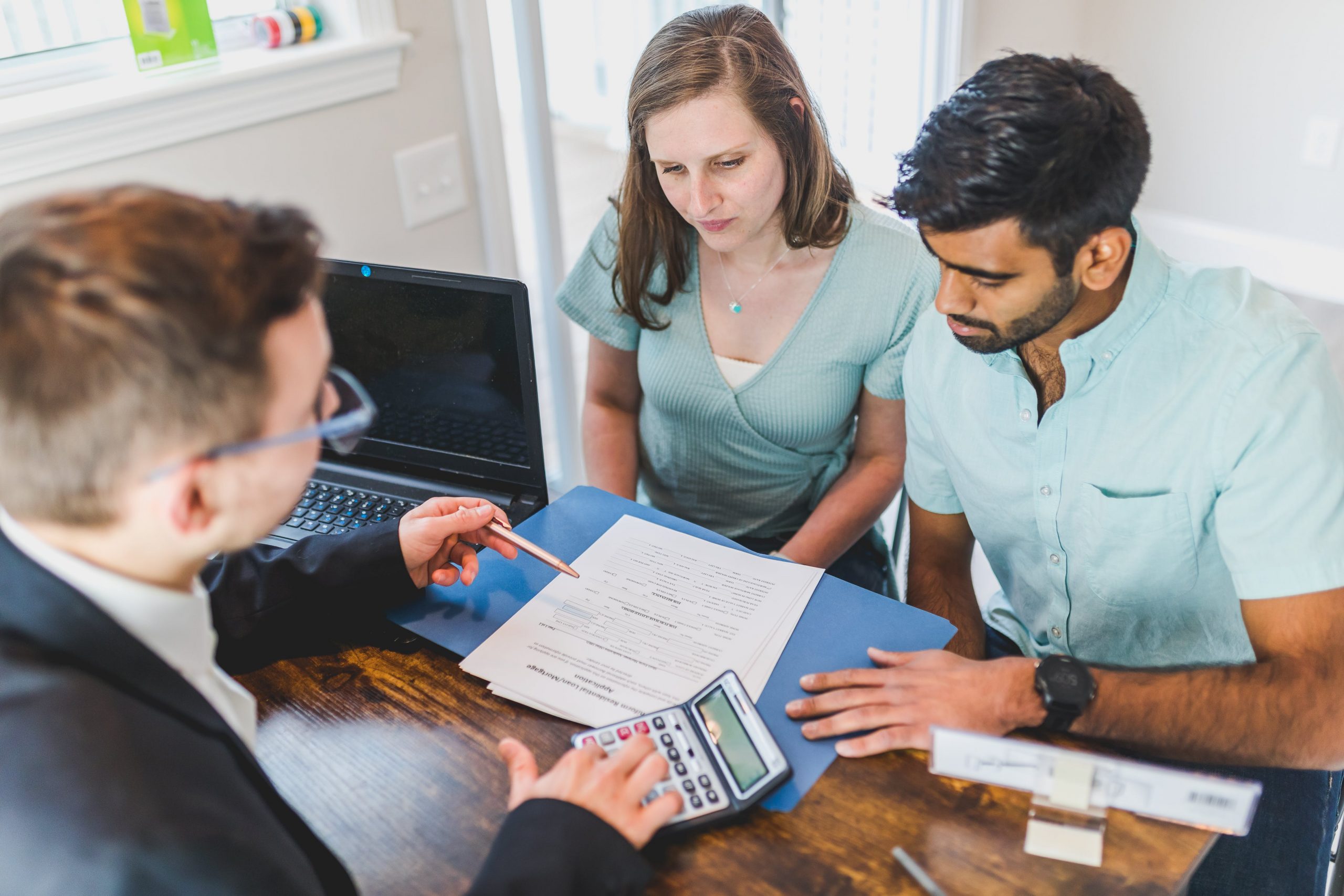 A loan officer reviews mortgage paperwork with two home buyers at a table with a calculator and laptop, how long it takes to close on a house in Greater Cincinnati, Kristine Green Realtor