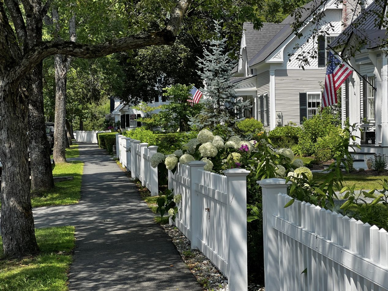 Tree-lined sidewalk with a white picket fence, evoking historic downtown Loveland, Ohio